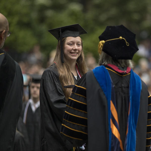 A student in her commencement regalia receives her degree from the president.