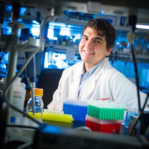 a male student in a lab coat smiles at the camera