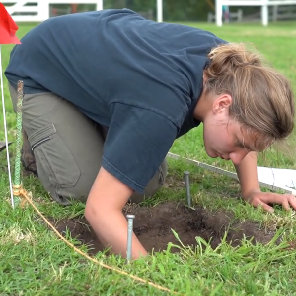 A student on her hands and knees excavates relics from a dig.