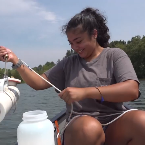 A young woman in a canoe lowers a water sampling device down into a lake.