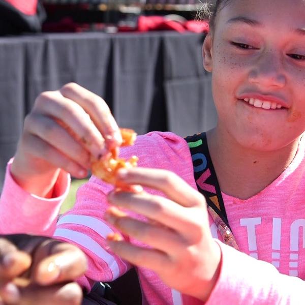 A young girl in a pink shirt excitedly peels a crawfish.