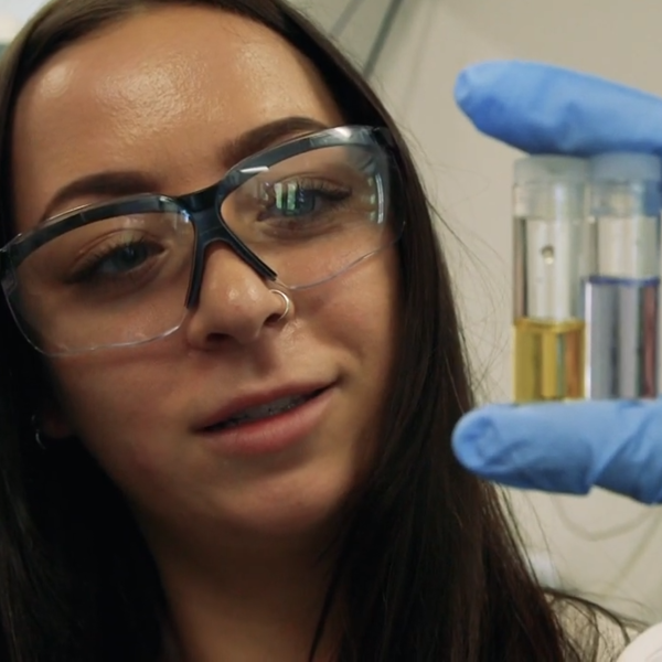 A woman in safety glasses inspects a pair of containers in her gloved hands.