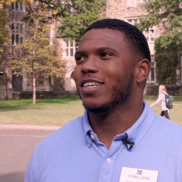 A young man in a blue button-down talks to the camera.
