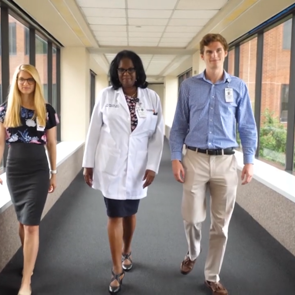 Two students flank a doctor as they walk through a hospital breezeway