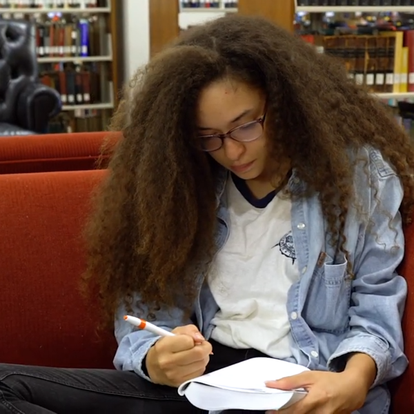 A young woman studies on a comfortable looking red couch in the library.