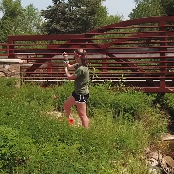 A young woman stands in reeds on a riverbank checking a water sample.