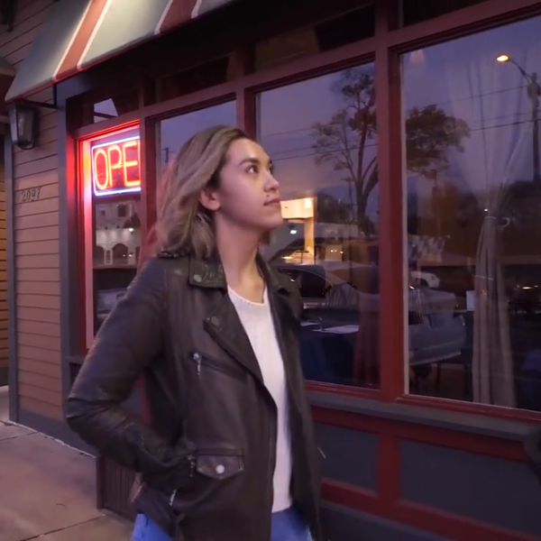 A young woman in a leather jacket walks in front of a row of restaurants.