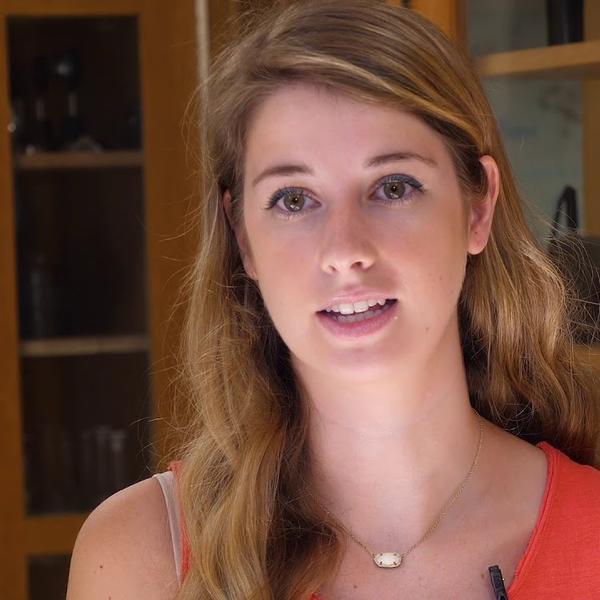 A young woman stands in a lab and addresses the camera.