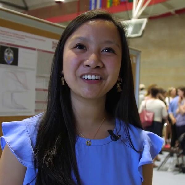 A dark haired young woman presents her research poster.