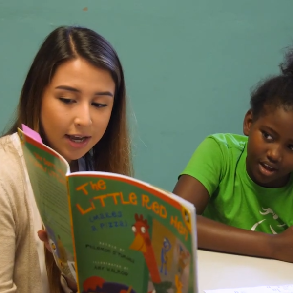 A young woman holds up and reads a book to a group of children.