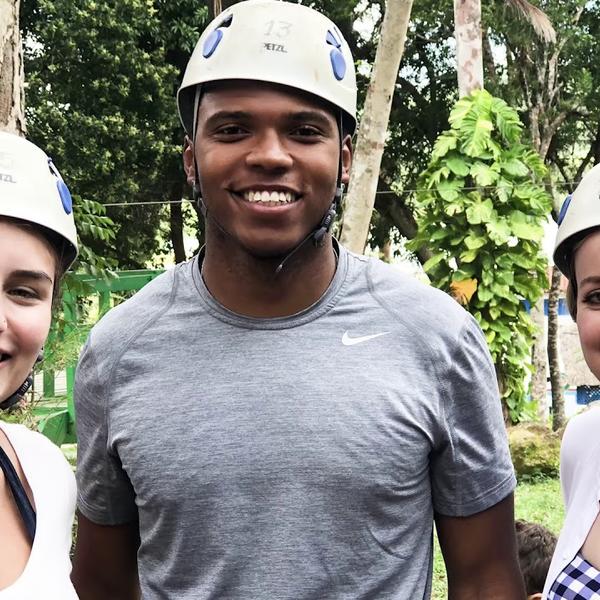 Three students in safety helmets pose for a photo with woods in the background.