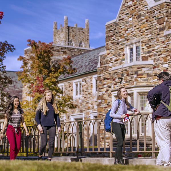 Groups of students congregate in front of a stone building.