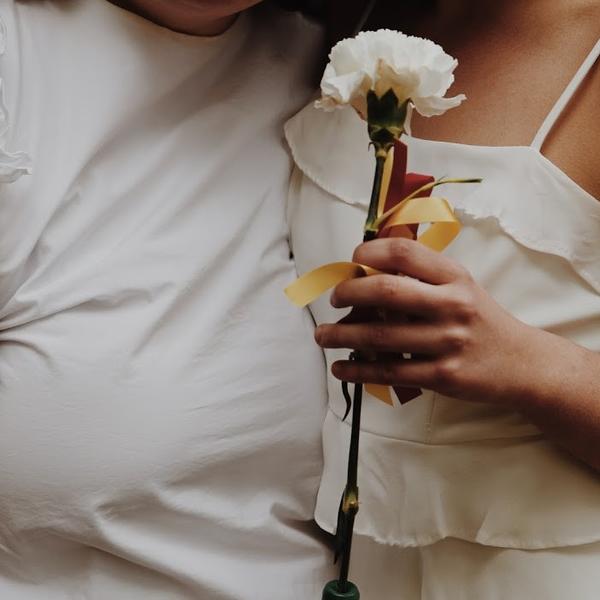 close up shot of two young women hugging, one holding a flower