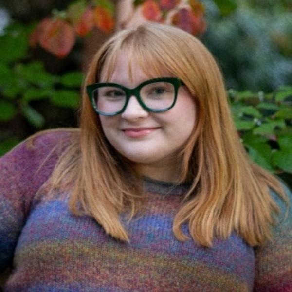 A woman with glasses and a striped sweater standing in front of flowers.