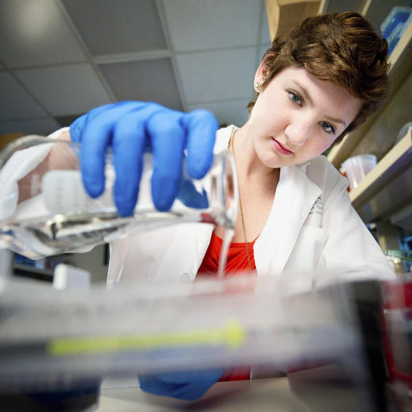 A woman with short brown hair measures liquid in a test tube.