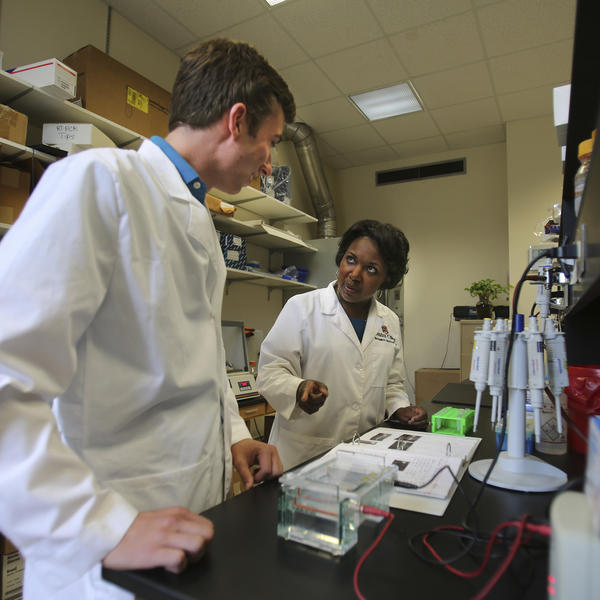 A student and professor stand at a chemistry workstation.