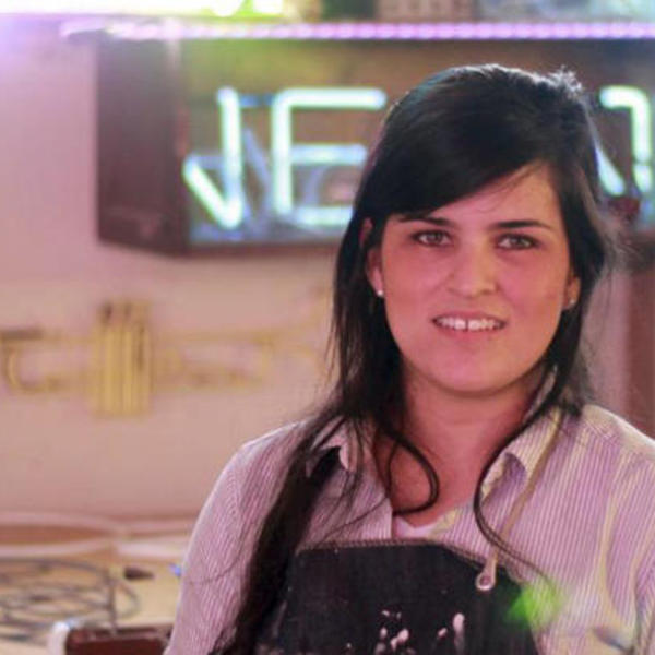 A woman stands in front of a neon sign.