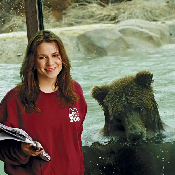 A student standing in front of a window. Behind them a grizzly bear is eating a fish.