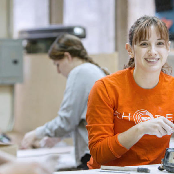 A young woman in an orange shirt sculpting.