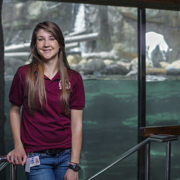 a young woman stands in front of a zoo exhibit with a polar bear