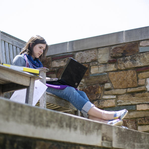 a female student sits on a bench and works on a laptop