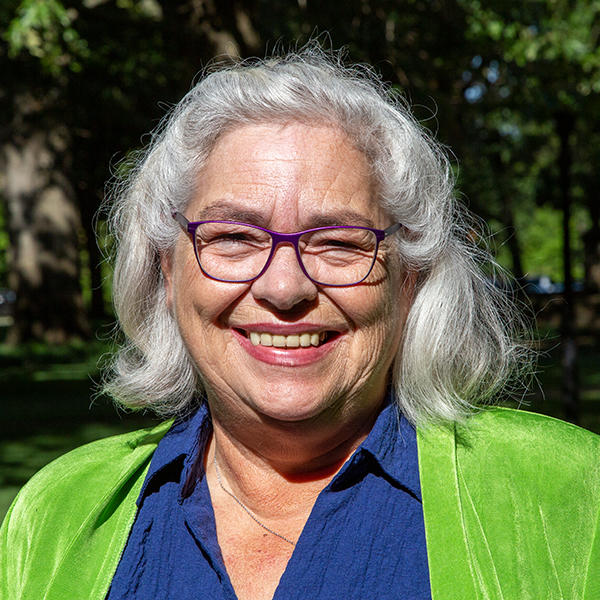 a woman with gray hair dressed in green smiles at the camera