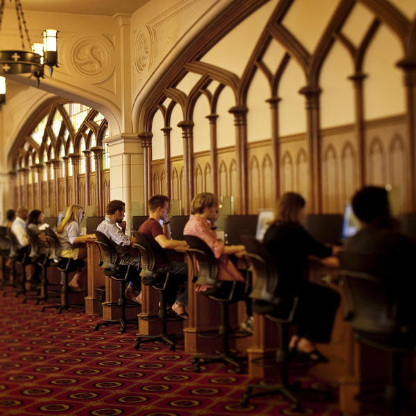 students sit at a bank of computers in a Gothic library