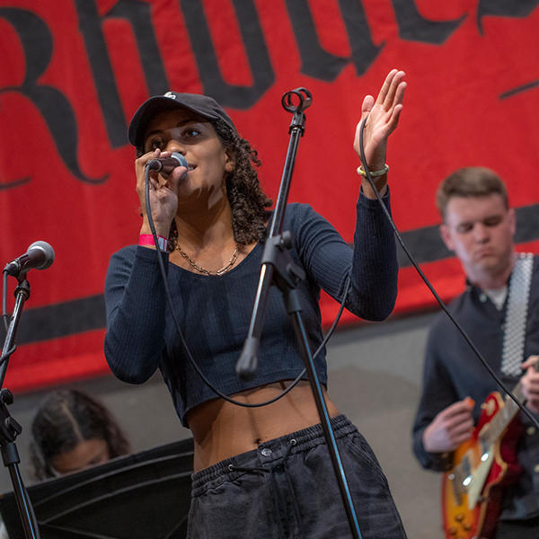 a young woman sings in front of a Rhodes banner