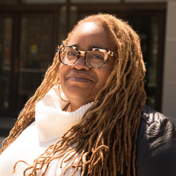 an African American woman with long hair and glasses smiles at the camera