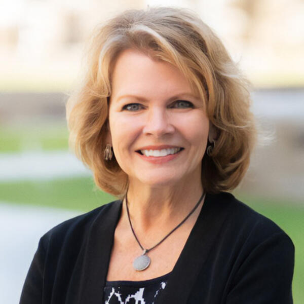 a woman in a dark colored suit smiles for the camera