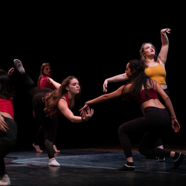 A group of women dance in a black-box theatre.