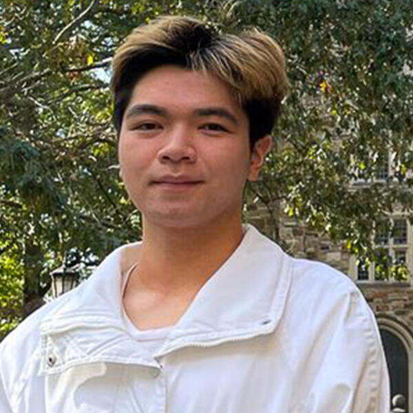 Male student in long-sleeve white shirt in front of a Gothic stone building