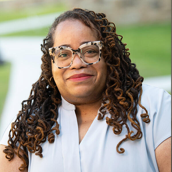 an African American woman with long hair and glasses smiles at the camera