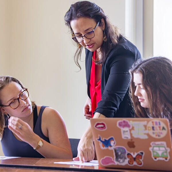 a female professor confers with students with lap tops