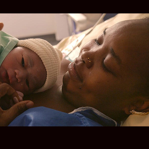 a mother smiles at a baby laying on her chest