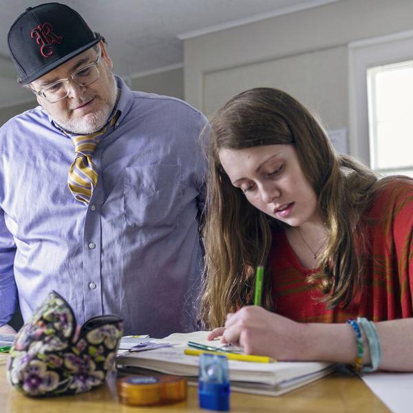 a professor looks on as a student writes on paper