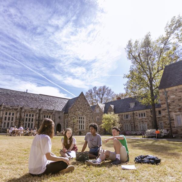 Students it on the grass outside a Rhodes building