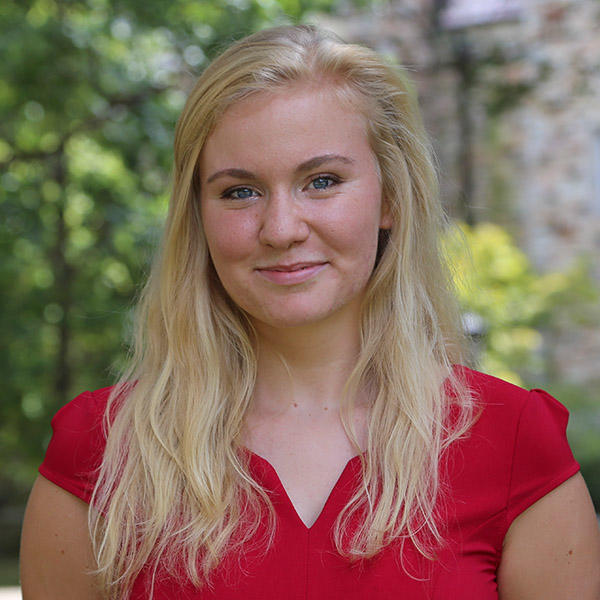A young blonde woman in a red top smiles into the camera.