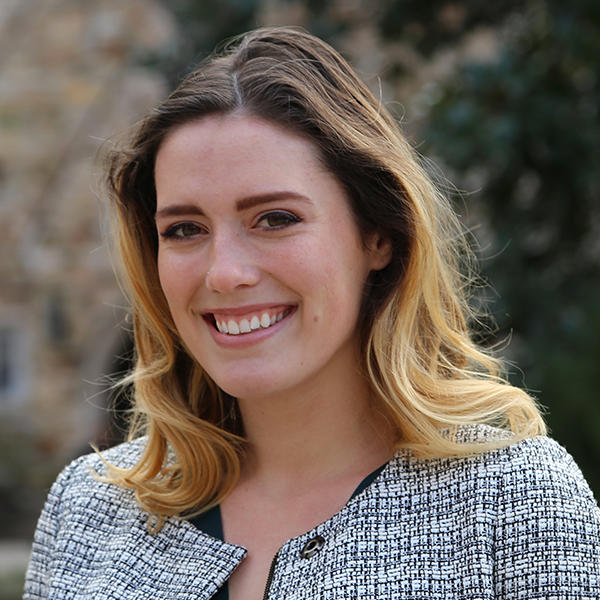 A young woman smiles in front of a stone building