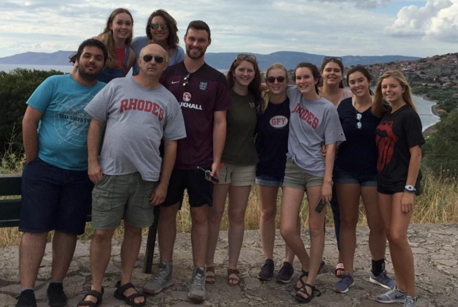 Photo of students and one male professor in shorts and t-shirts in front of water and hills in Greece