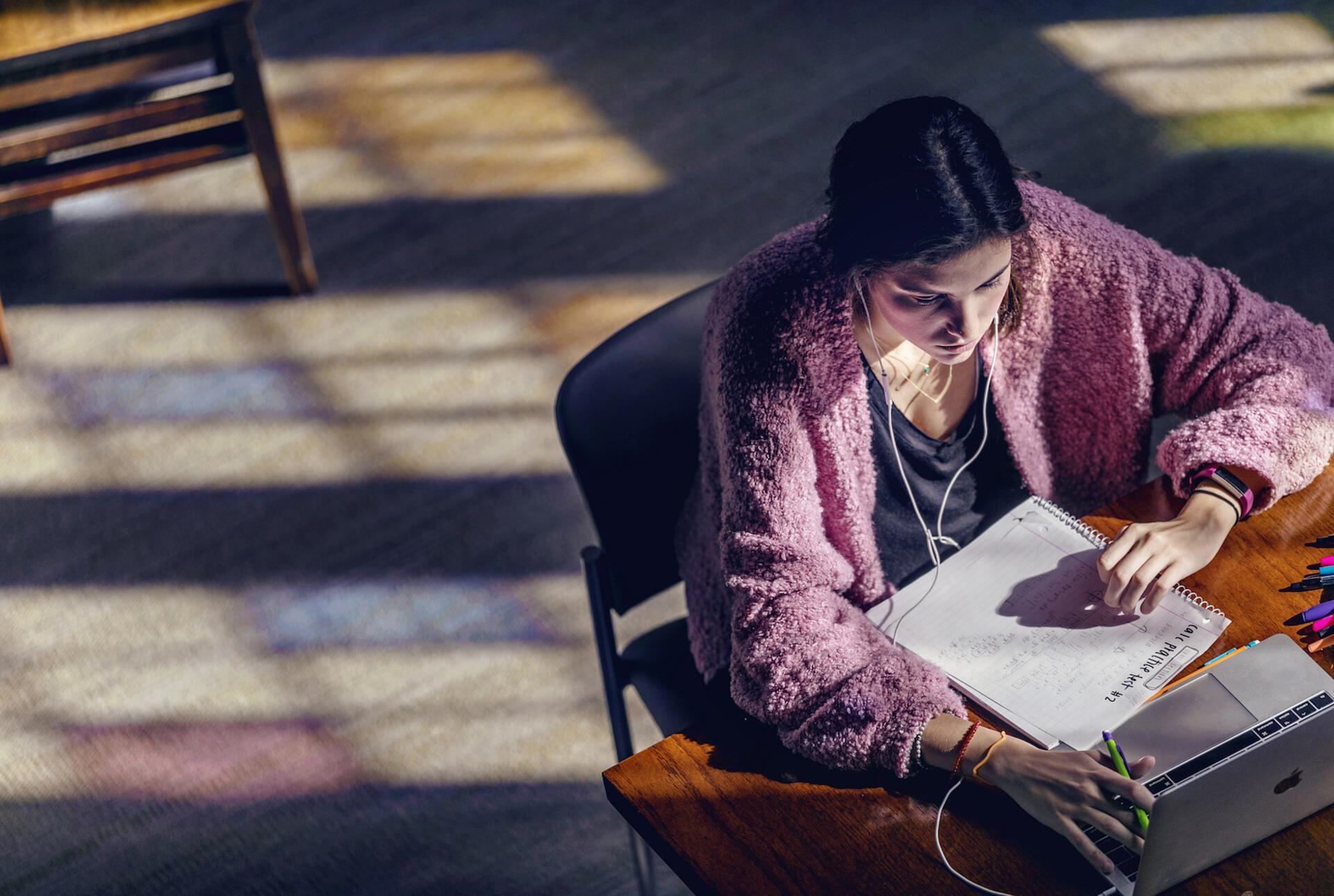 A girl sits in the library reading a paper as the afternoon light streams in from the stained glass windows.