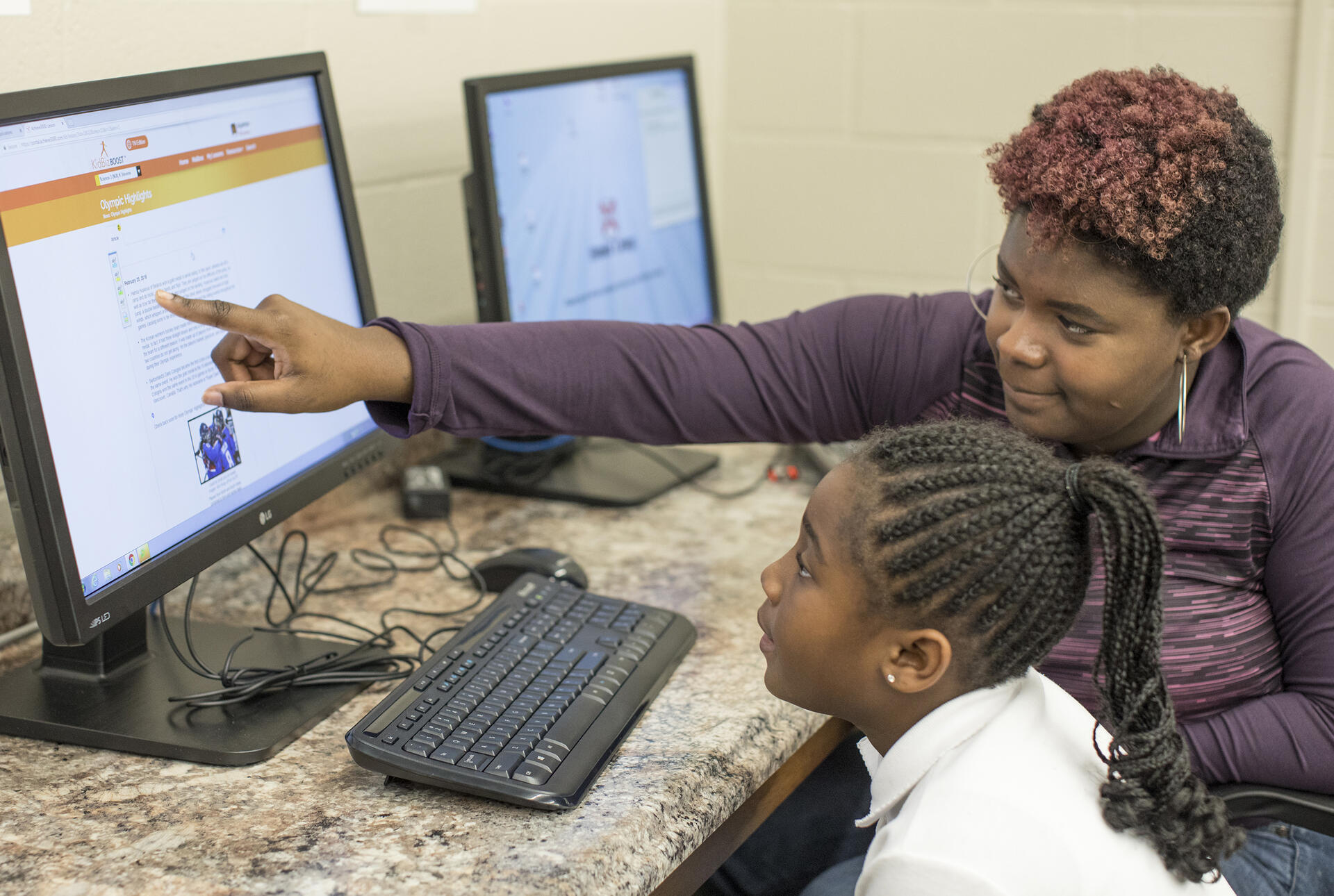 a college student helps a young girl at a computer