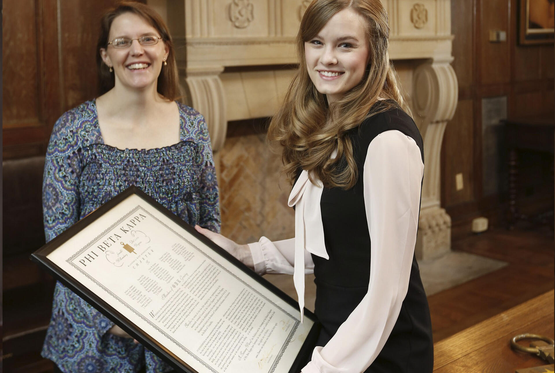 a student holds a Phi Beta Kappa certificate while a professor looks on