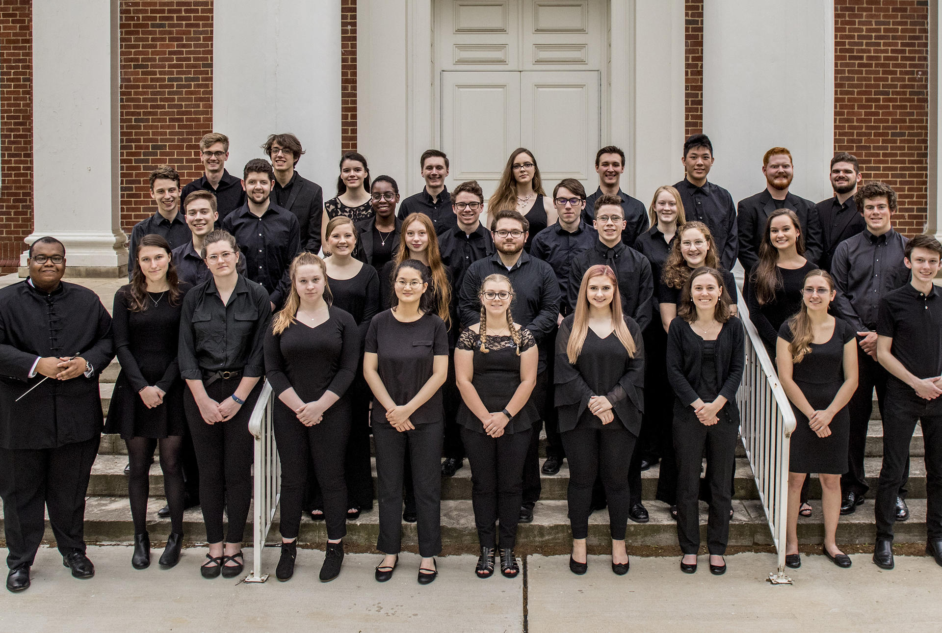 an orchestra poses on the steps of a concert hall