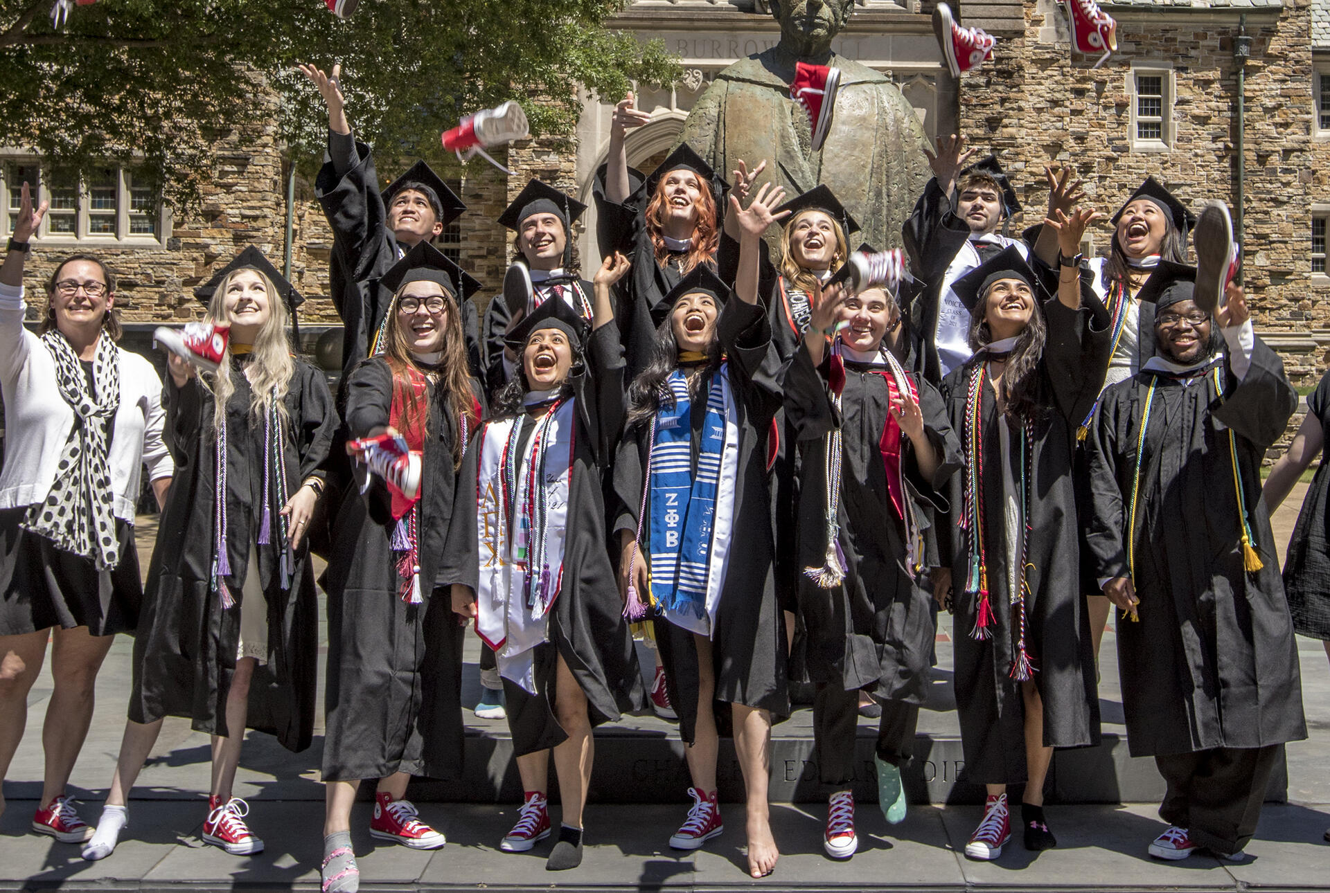 students in graduation robes toss red tennis shoes into the air