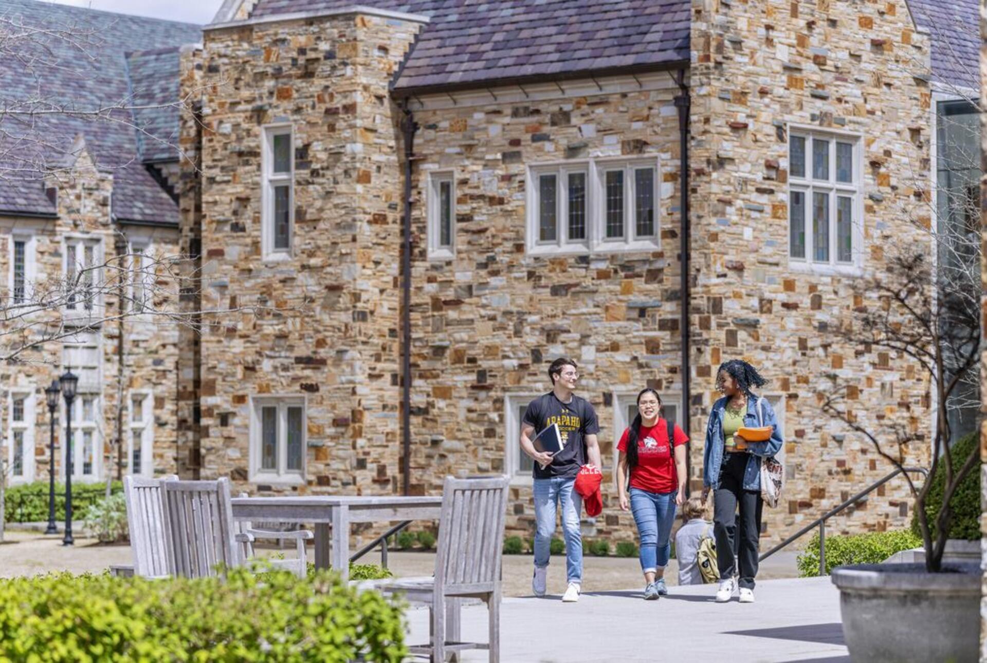 A group of three students on a spacious walkway with a two-story, collegiate gothic building in the background.