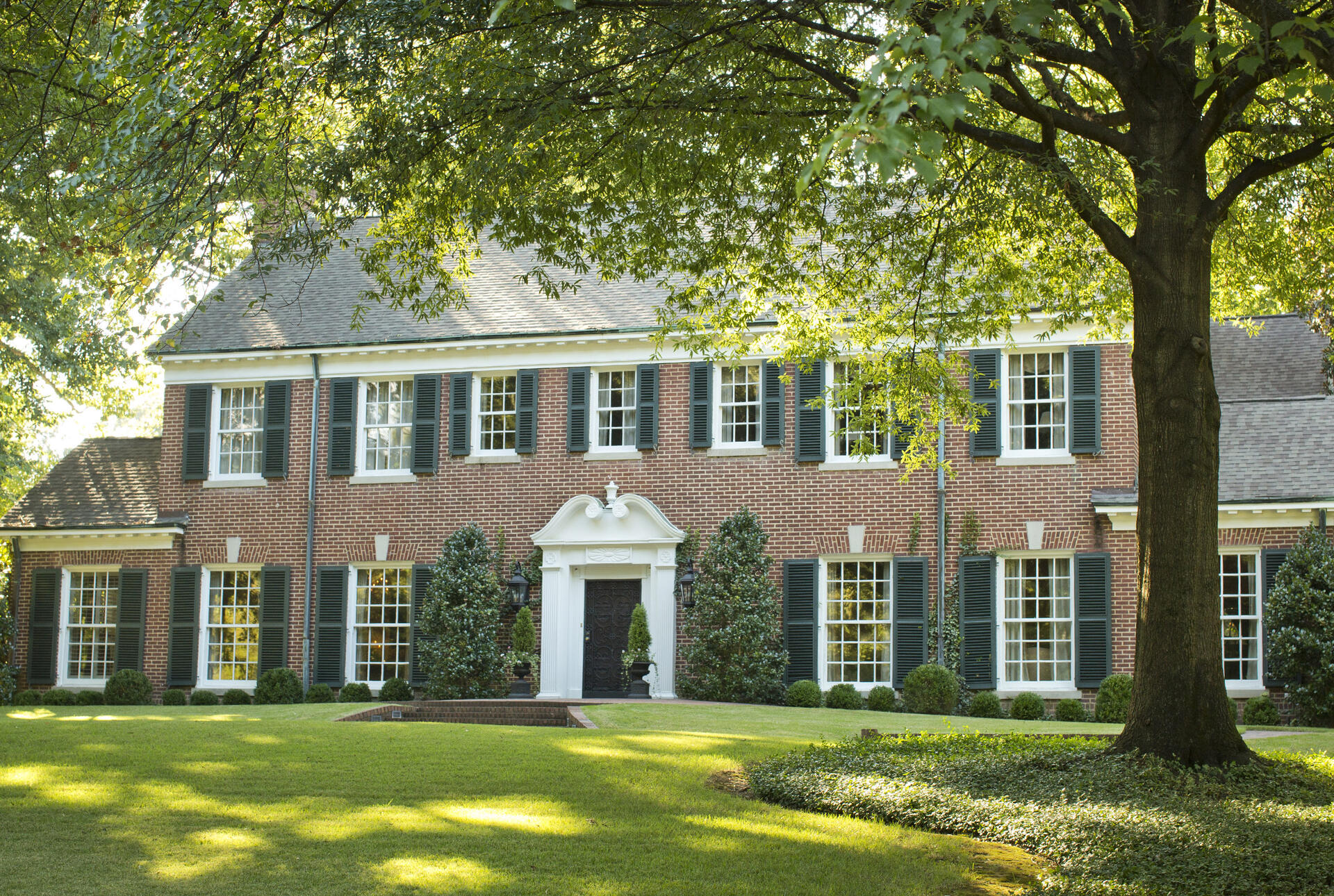 A red brick Georgian style home shaded by trees