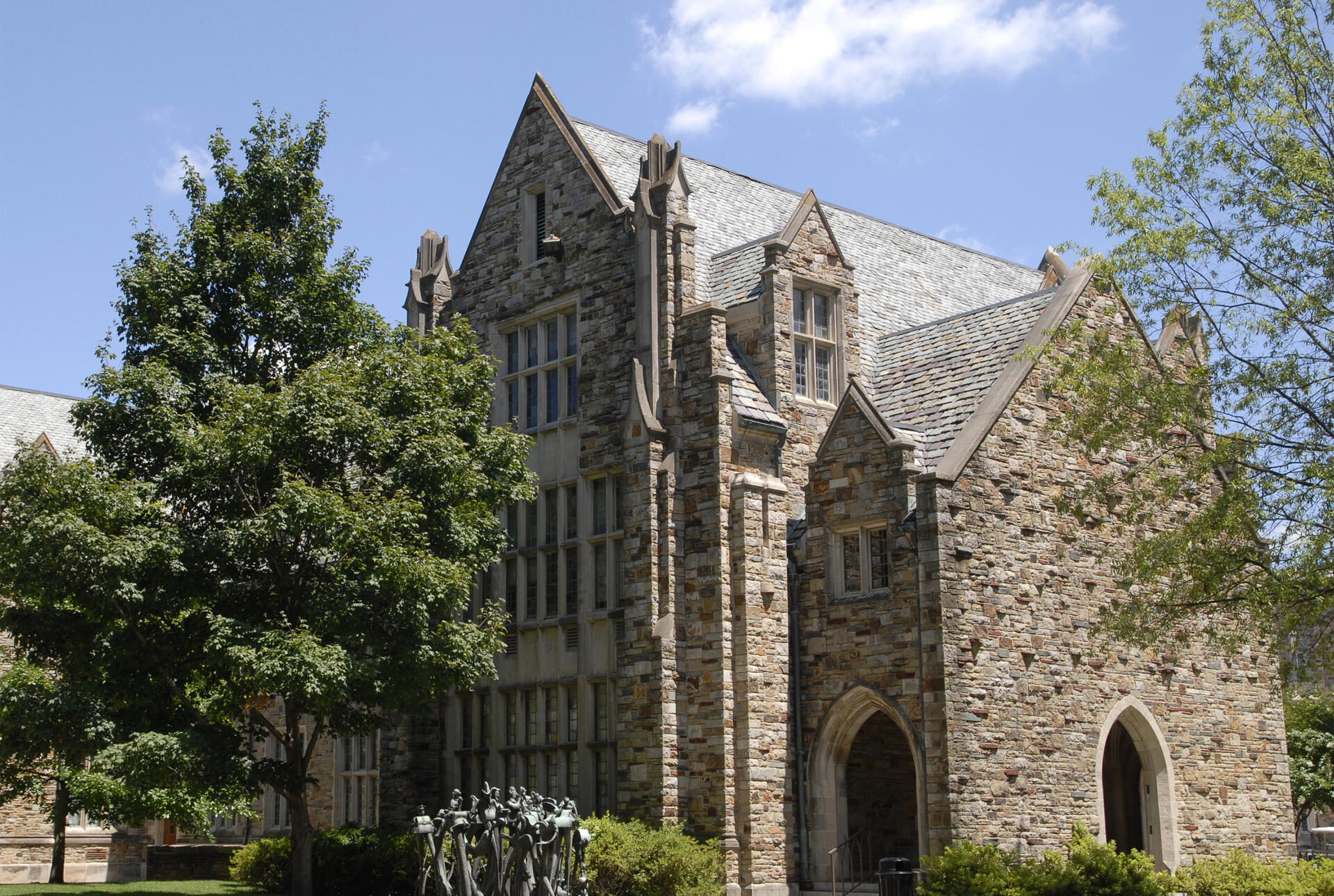 A stone edifice rises from behind some trees.