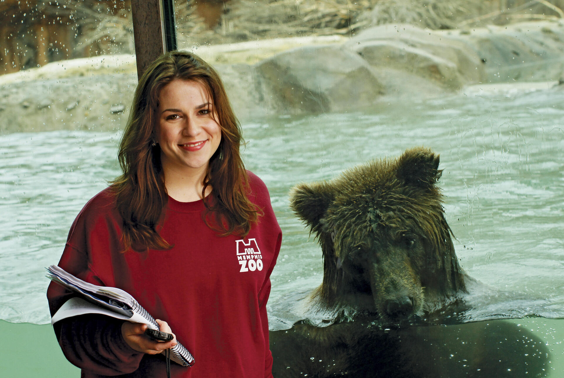 A young woman with a clipboard stands in front of a grizzly bear.