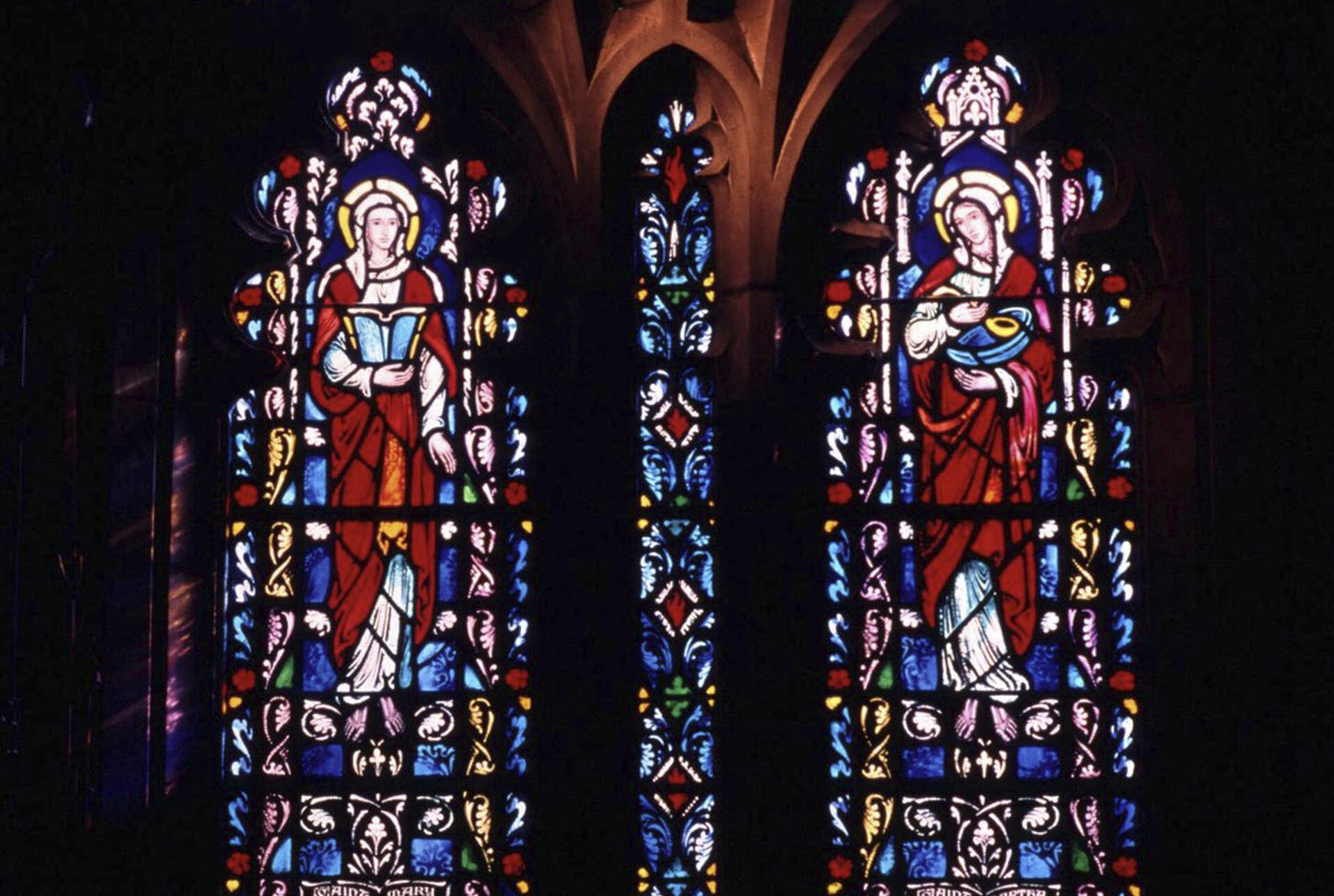 Two panels of stained glass featuring Mary Magdalene and Mary, mother of Jesus on a stone chapel wall